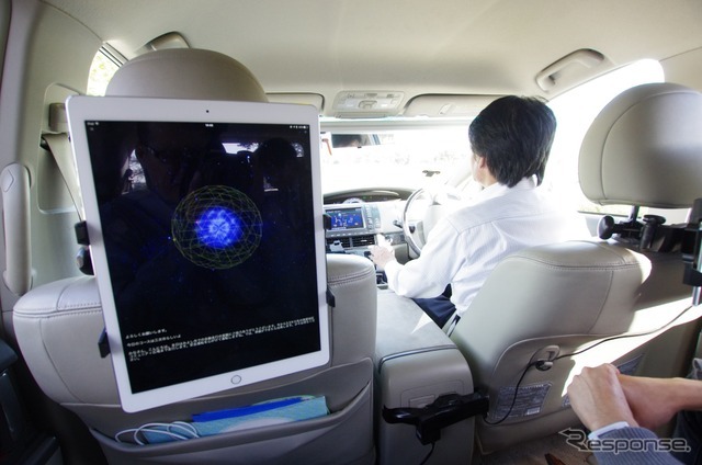 iPadのアプリとして稼働している「cocoro Drive」。色の付いた球体と、その回りのワイヤーフレームが感情を表現している。運転手は自動運転中だ。　《撮影　山田正昭》